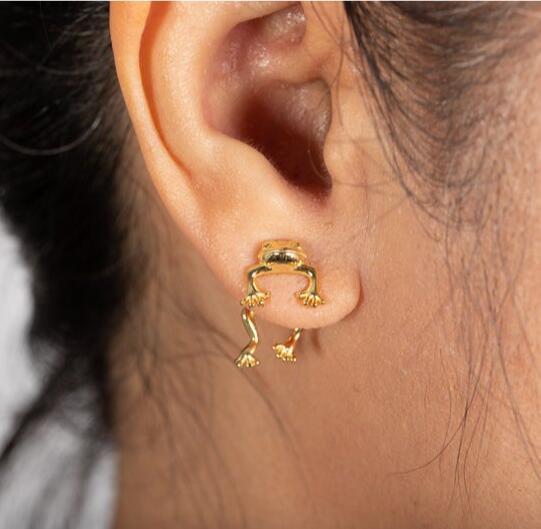 Gold frog-shaped earring worn on an ear with a neutral background