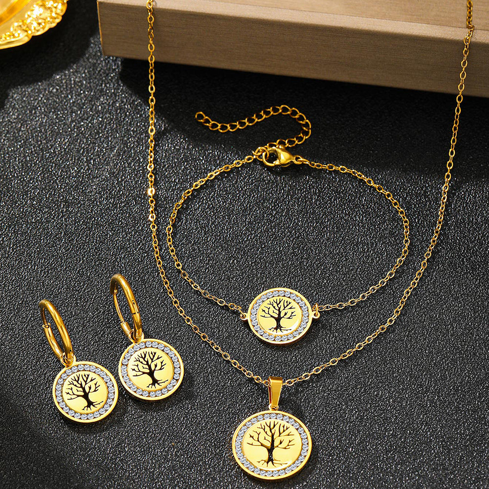 Gold jewelry set with tree of life pendants on a dark surface