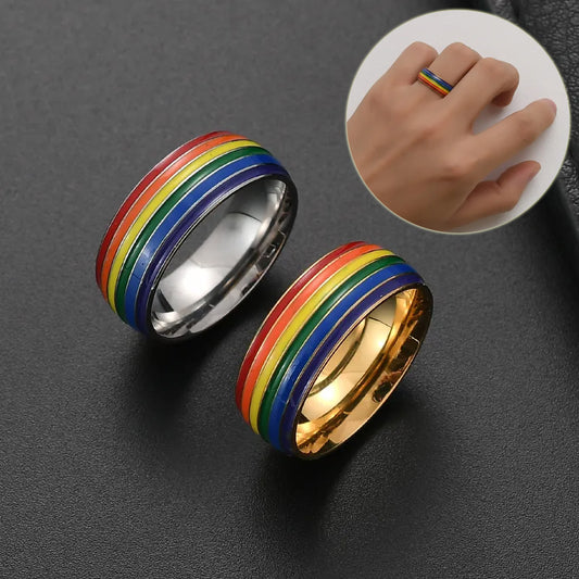 Two rainbow-striped rings, one silver and one gold, on a dark surface with a hand wearing a ring inset.