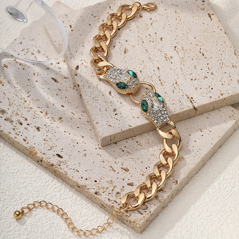 Gold chain bracelet with green gemstones on a textured stone surface