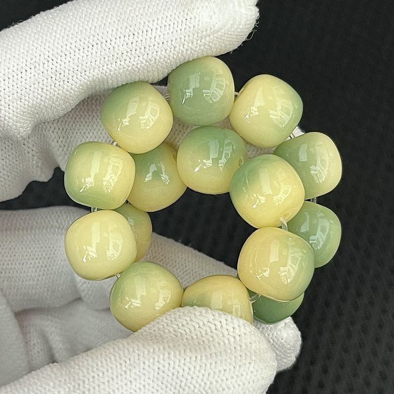 Green beaded bracelet held by a gloved hand against a dark background