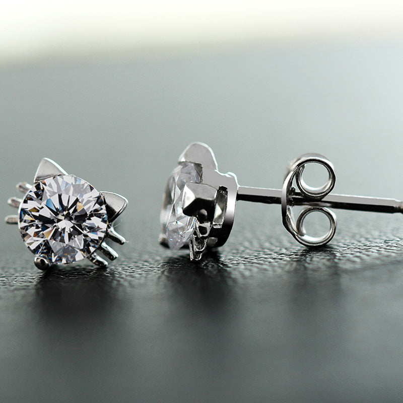 Pair of silver stud earrings with clear gemstones on a reflective surface.