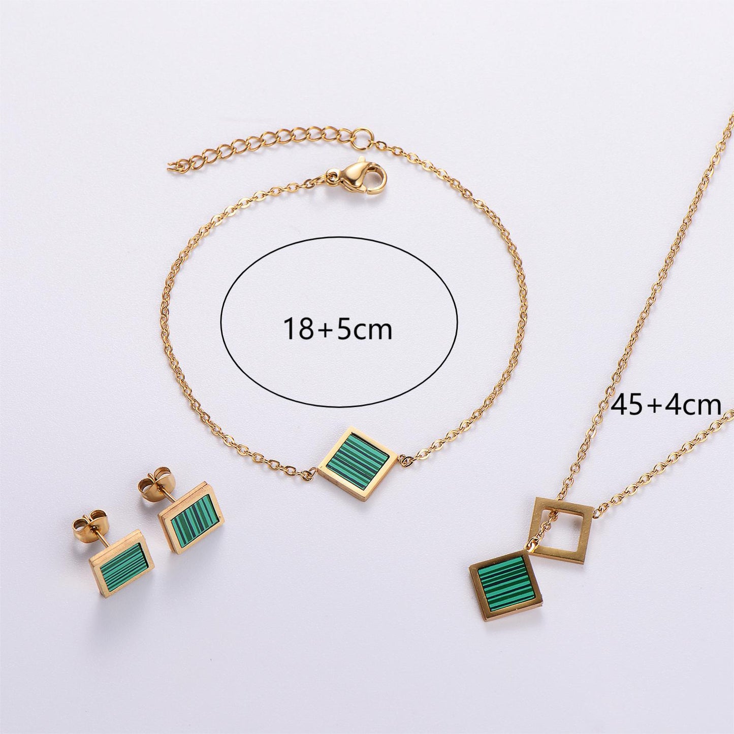 Gold jewelry set with green square pendants on a white background