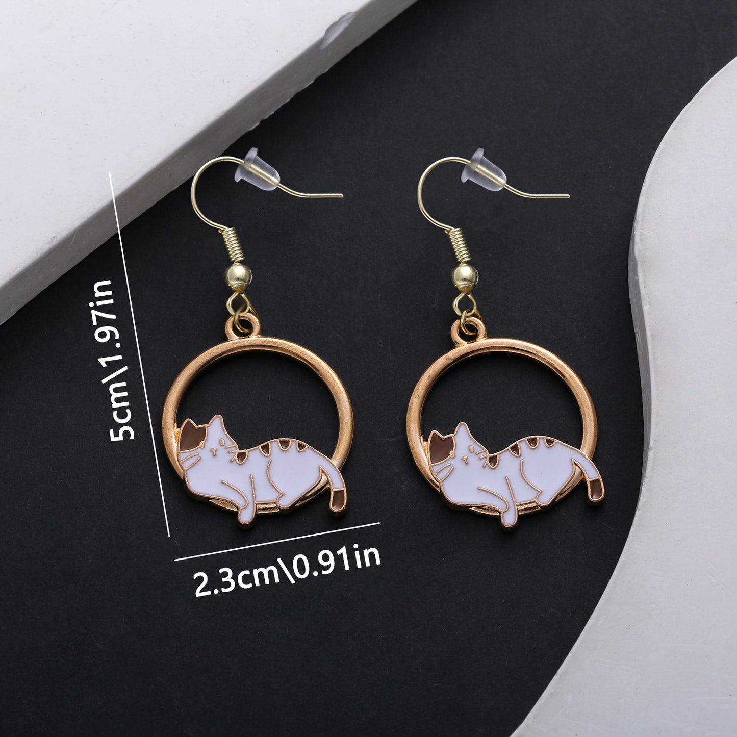 Cat-shaped earrings with gold circular design on a black background with measurements.