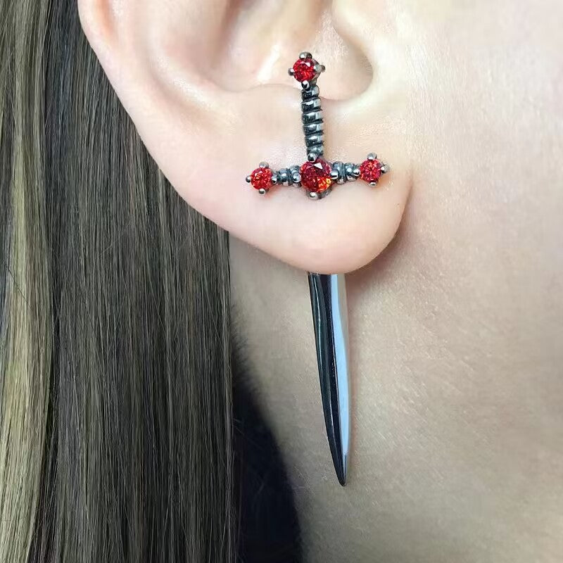 Earring with red gemstones and a long black spike on an ear.
