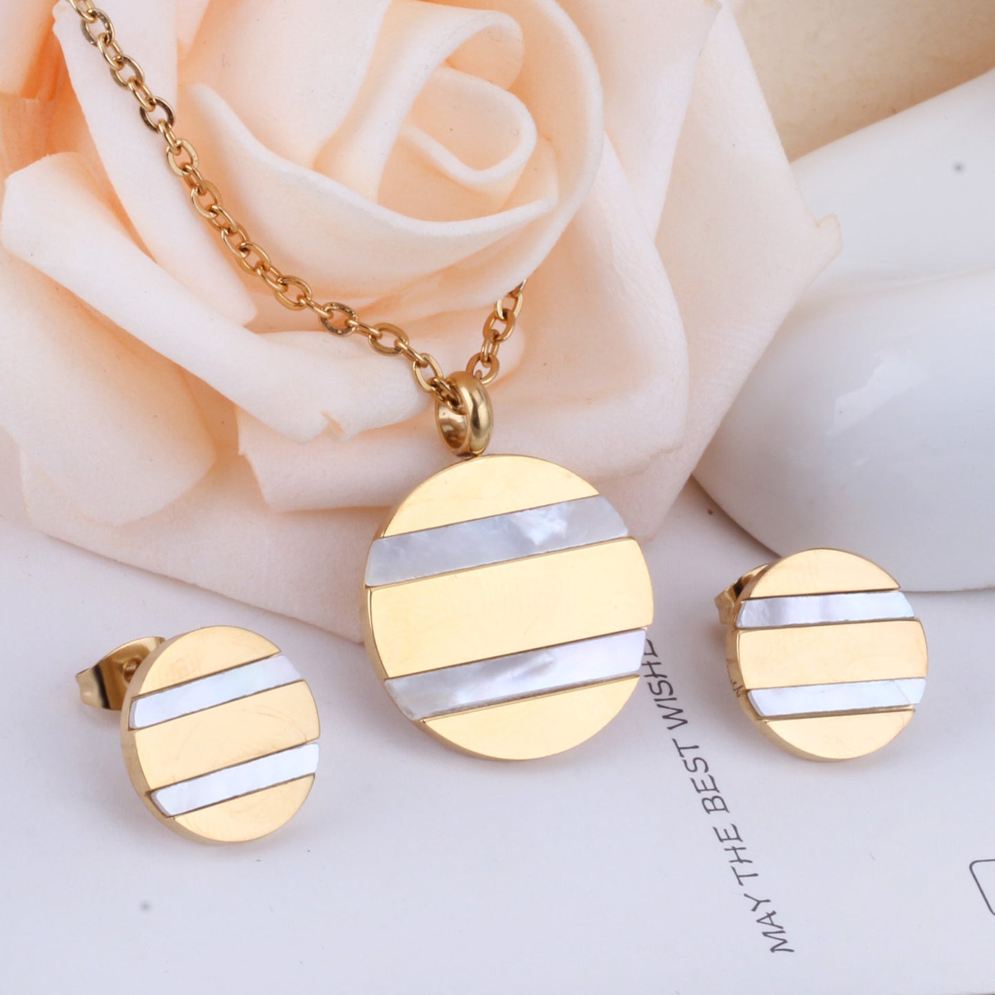 Gold and silver circular earrings on a white surface with a rose in the background
