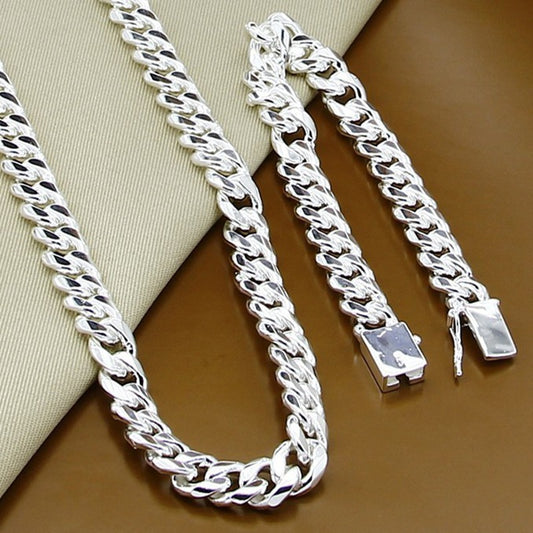 Two silver chain necklaces on a brown surface with a beige fabric background.
