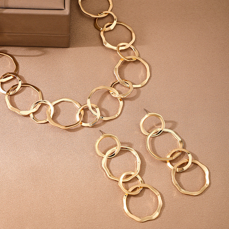 Gold chain necklace and earrings on a beige surface