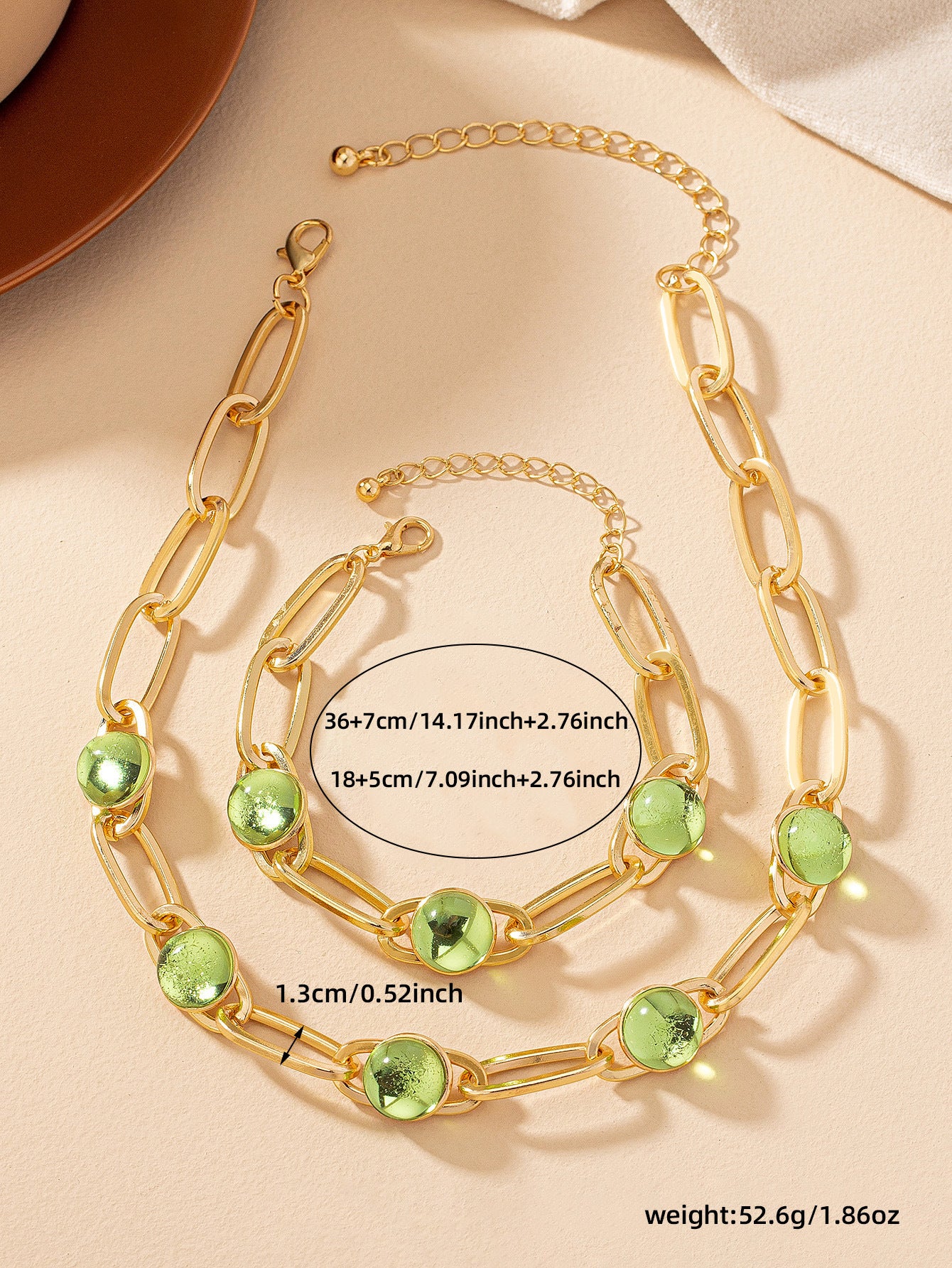 Gold chain necklace with green gemstones on a beige background