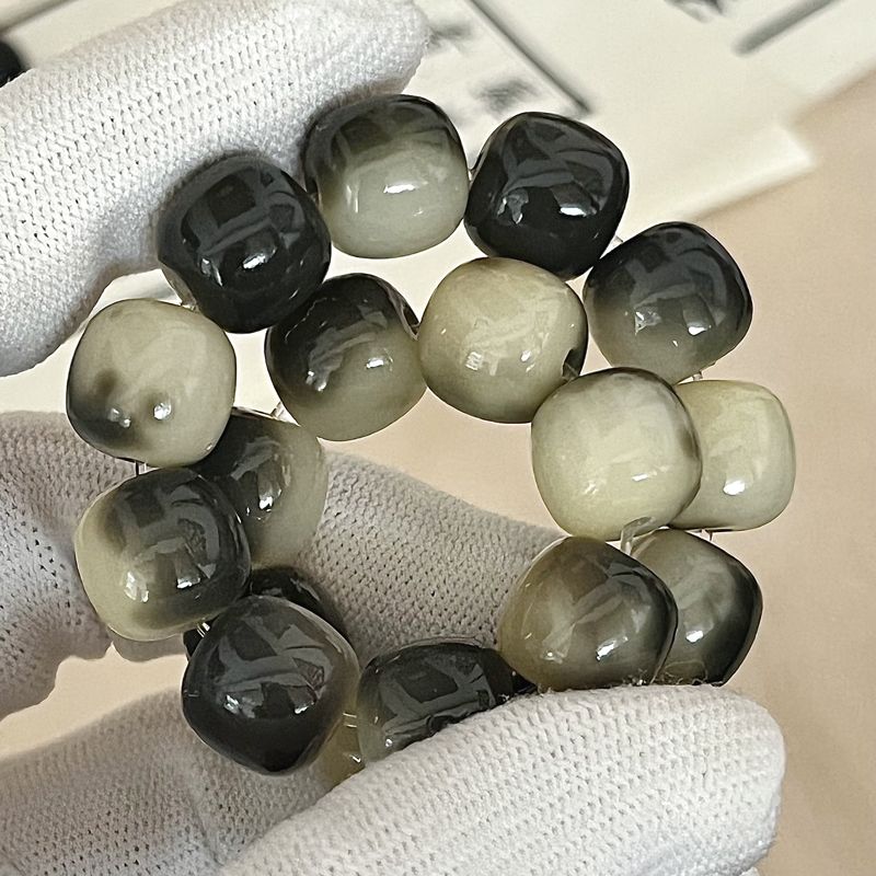Necklace with dark and light green beads held by a gloved hand on a neutral background