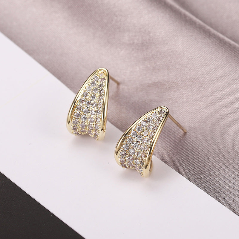 Gold earrings with diamond accents on a soft fabric background