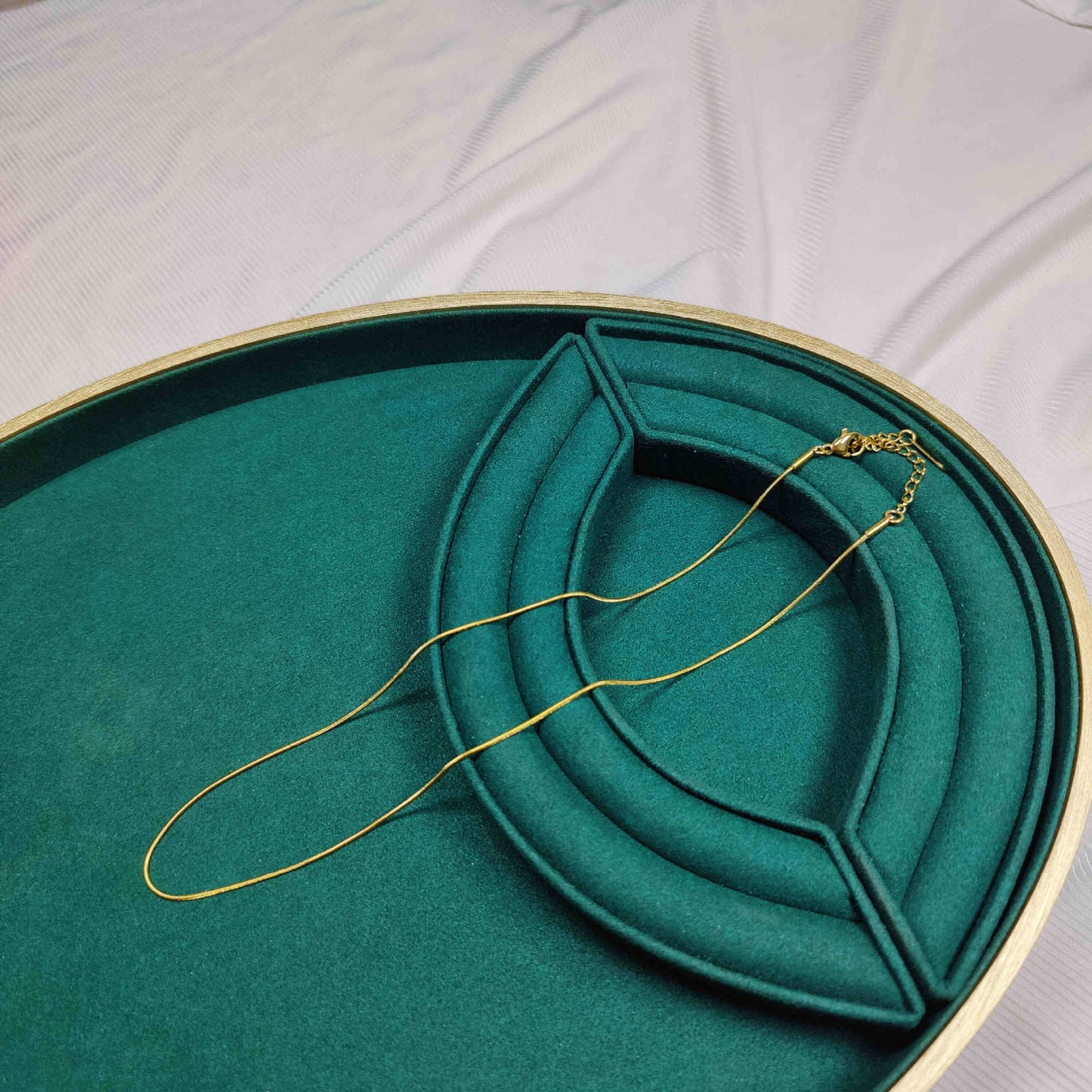 Gold necklace on a green jewelry box with a white fabric background