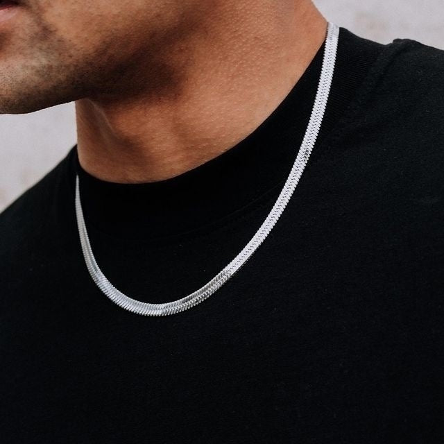 Silver chain necklace worn by a person on a black shirt with a neutral background