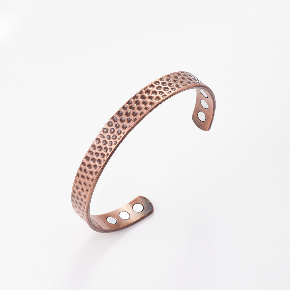 Rose gold bracelet with textured surface and circular cutouts on a white background