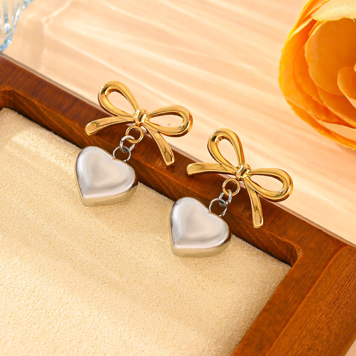 Gold bow and heart-shaped earrings on a wooden tray with a soft background