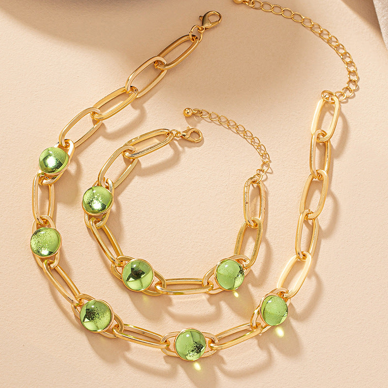 Gold chain necklace with green gemstones on a beige background