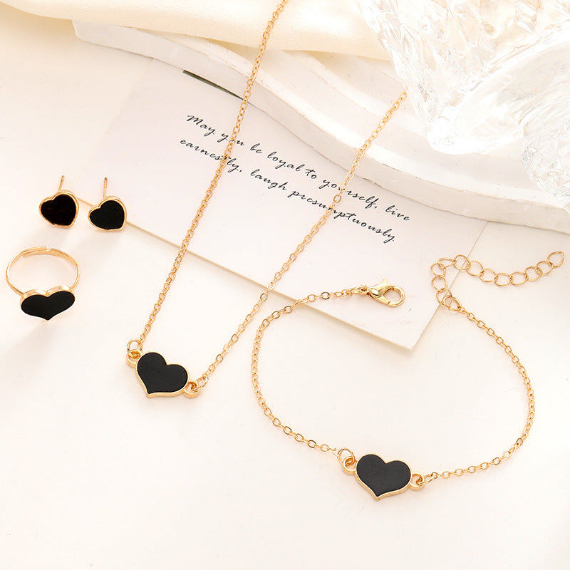 Gold jewelry set with black heart charms on a white surface