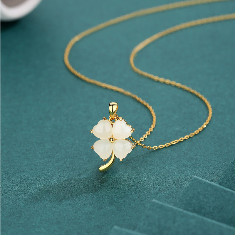 Gold necklace with a four-leaf clover pendant on a teal background