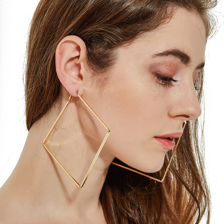 Close-up of a woman wearing gold geometric hoop earrings on a white background