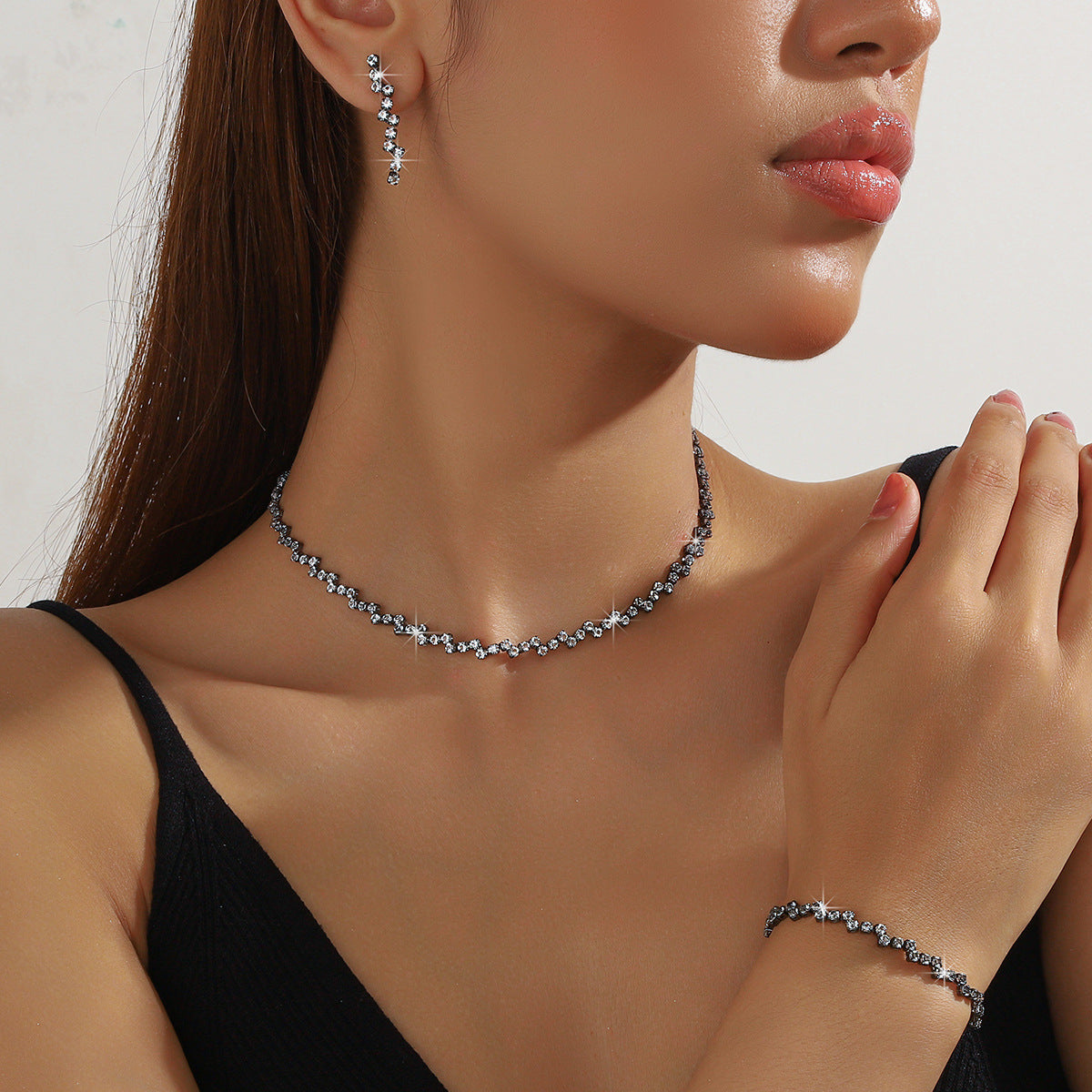 Close-up of a woman wearing a necklace, earrings, and bracelet against a neutral background