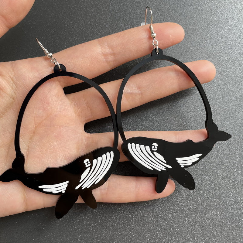 Black hoop earrings with white accents held in a hand against a gray background