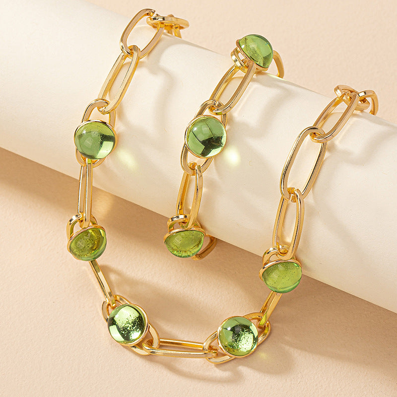 Gold chain bracelet with green gemstones on a beige background