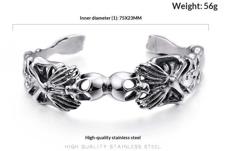 A silver-toned stainless steel cuff bracelet with detailed skull and crossbones motifs on each side, shown on a white background with text overlays indicating inner diameter and weight.