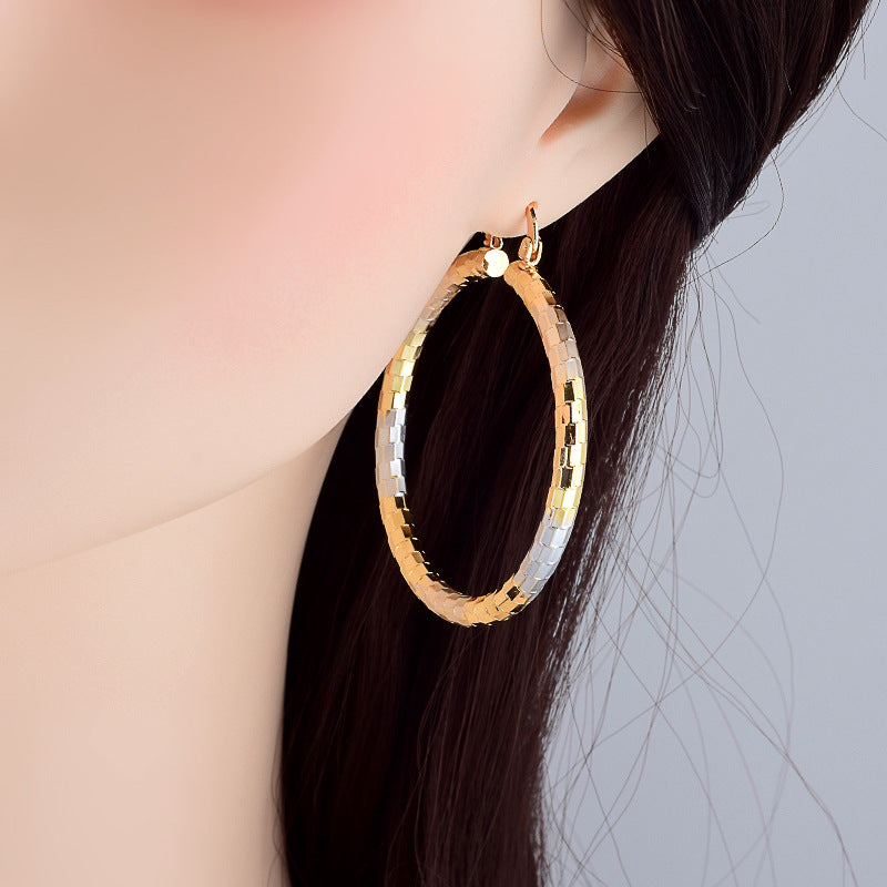 Gold hoop earring worn by a person with dark hair against a neutral background