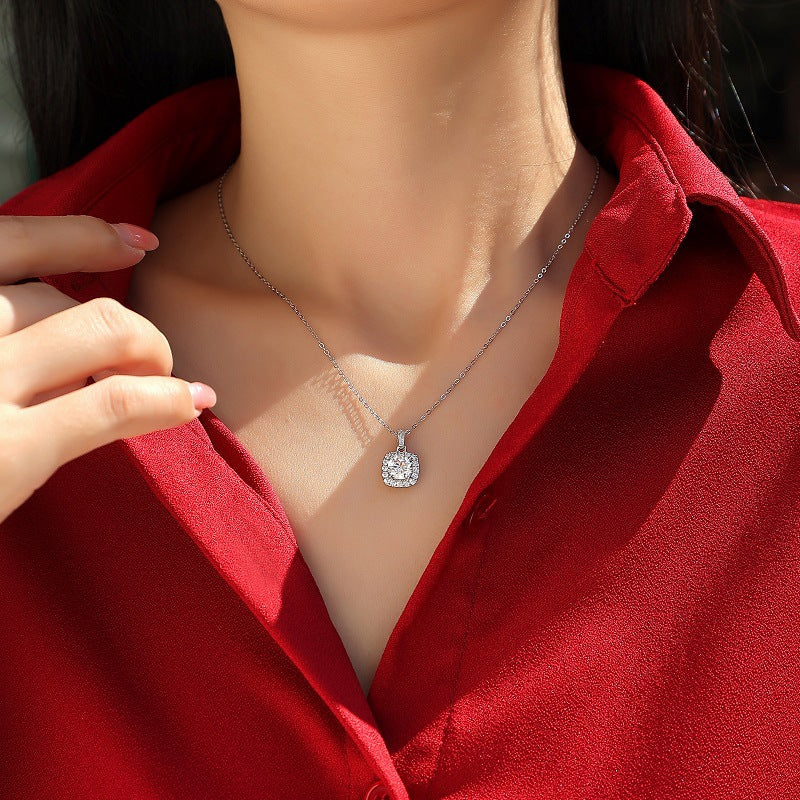 Person wearing a silver necklace with a diamond pendant against a red shirt.