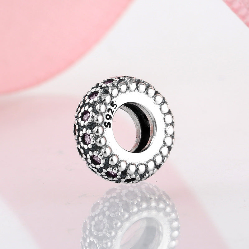 Silver charm with pink gemstone on a pink background