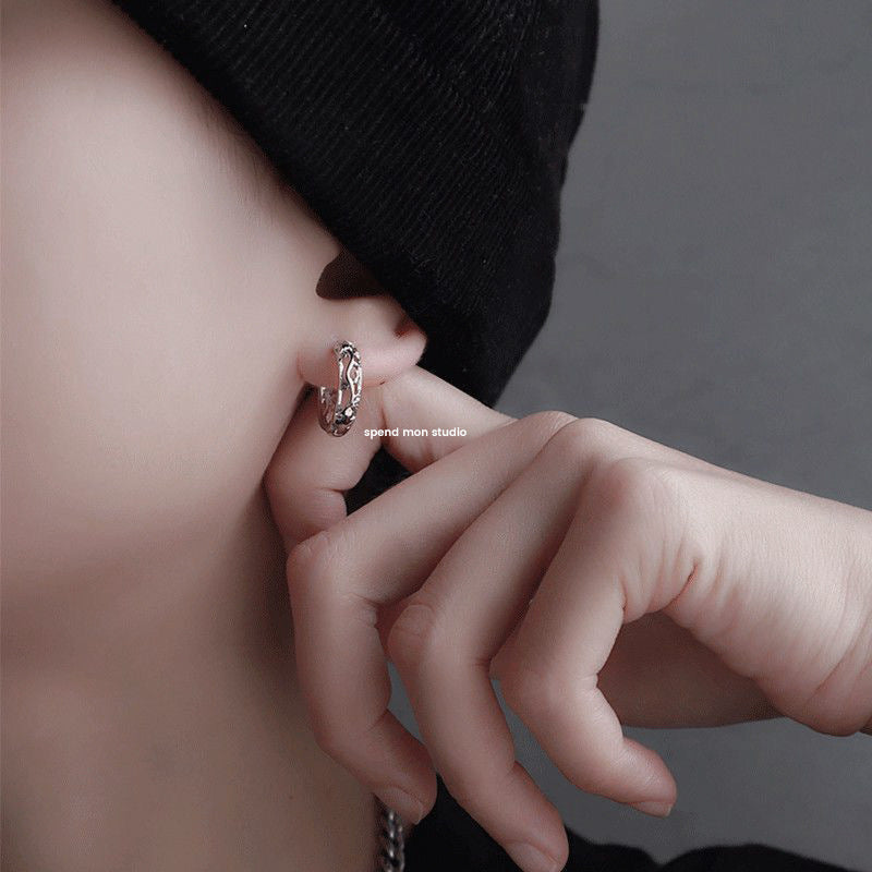 Close-up of an ear with a silver earring, hand adjusting it against a neutral background.