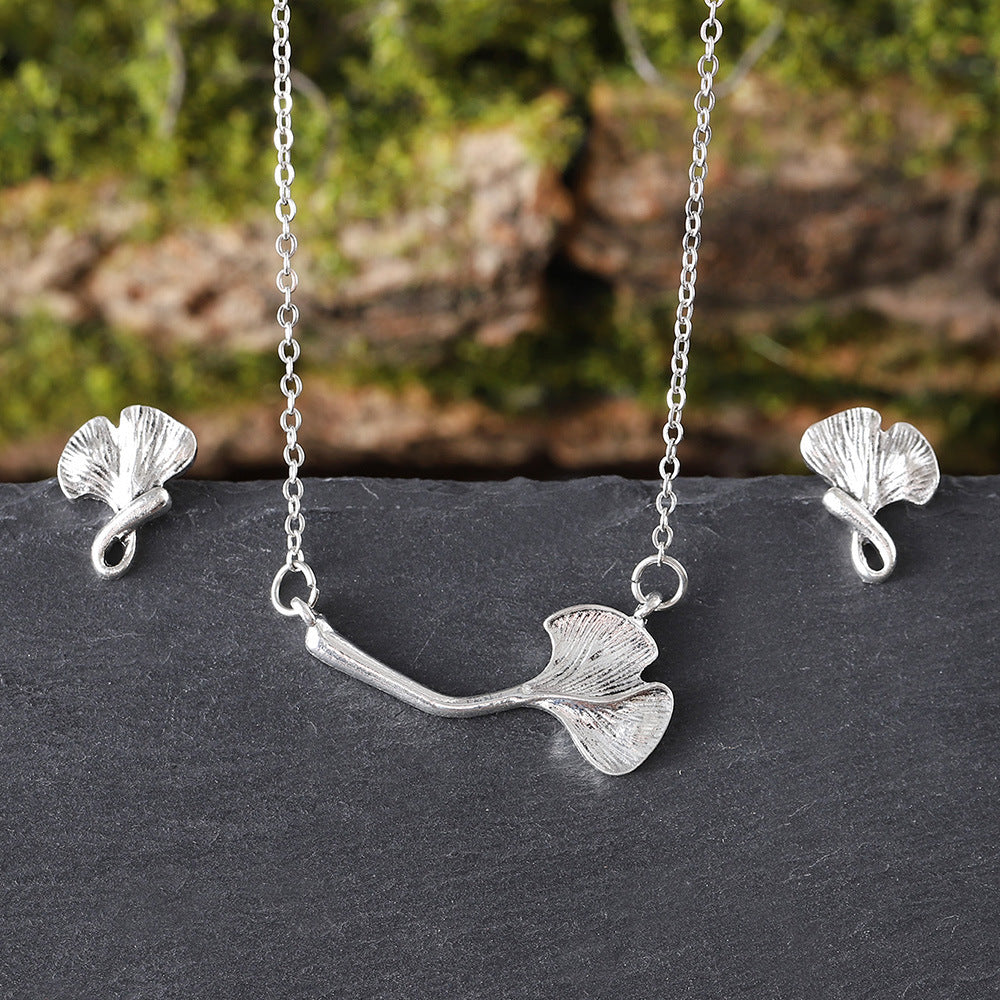 Silver ginkgo leaf necklace and earrings on a dark surface with a natural background