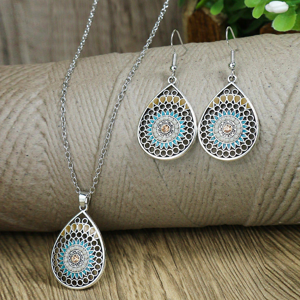 Jewelry set with teardrop-shaped pendant and matching earrings on a wooden surface.