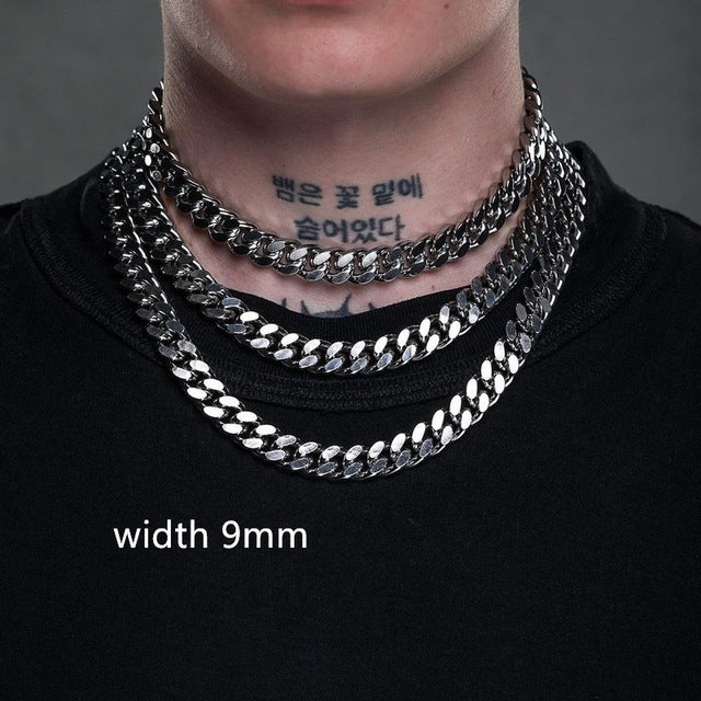 Person wearing a stack of silver chain necklaces with visible tattoos on a dark background.
