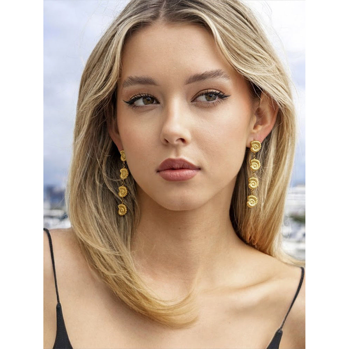 Woman wearing gold earrings with a blurred outdoor background