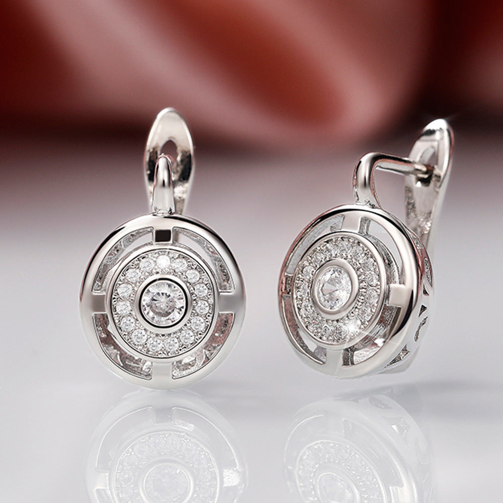Pair of silver earrings with diamond accents on a reflective surface.
