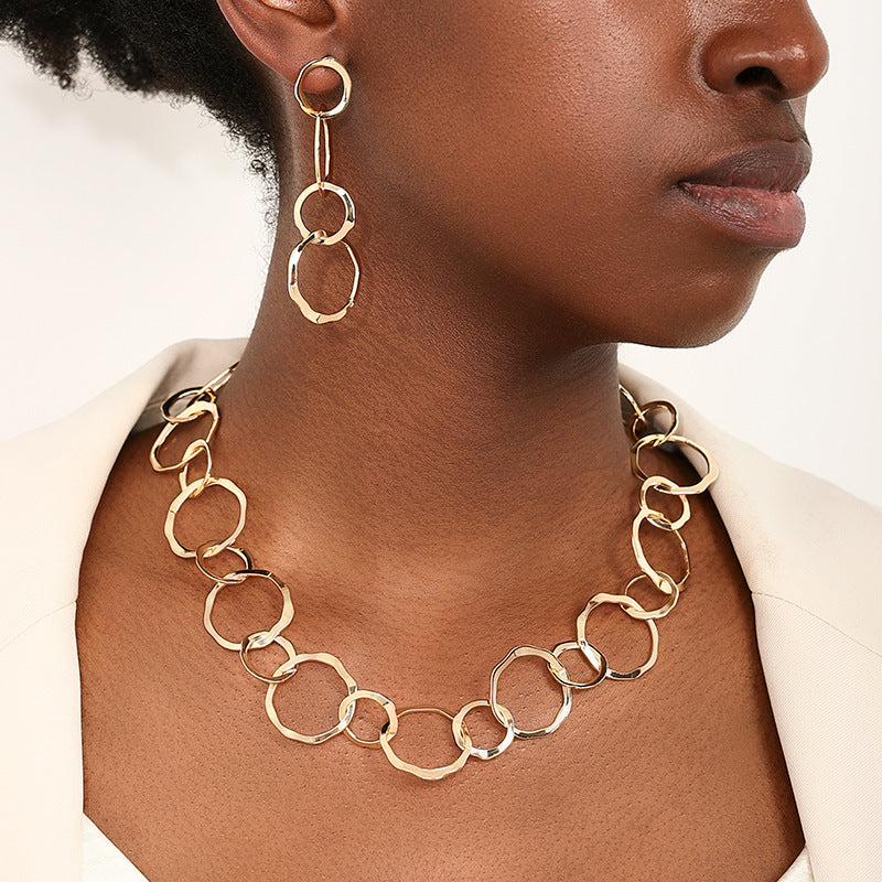 Gold chain necklace and earrings on a person against a neutral background