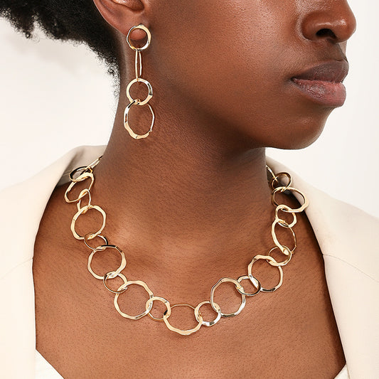 Gold chain necklace and earrings on a person against a neutral background