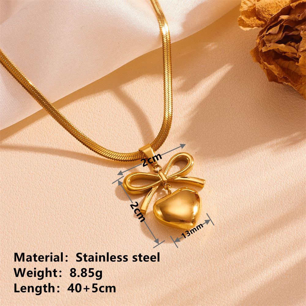 Gold necklace with heart and bow pendant on a beige fabric background