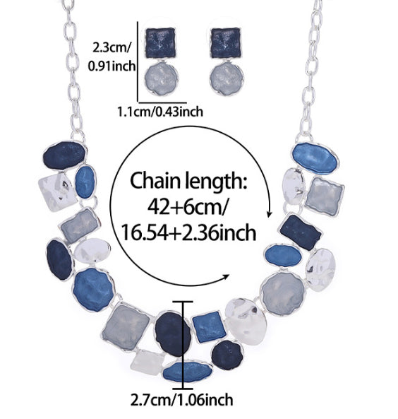 Silver statement necklace with irregular blue, navy, gray, and white stones, shown with chain length measurements and matching stud earrings on a white background.